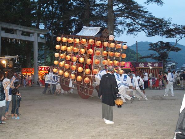 神社の境内に提灯を灯した山車を男性陣が担いで到着した写真